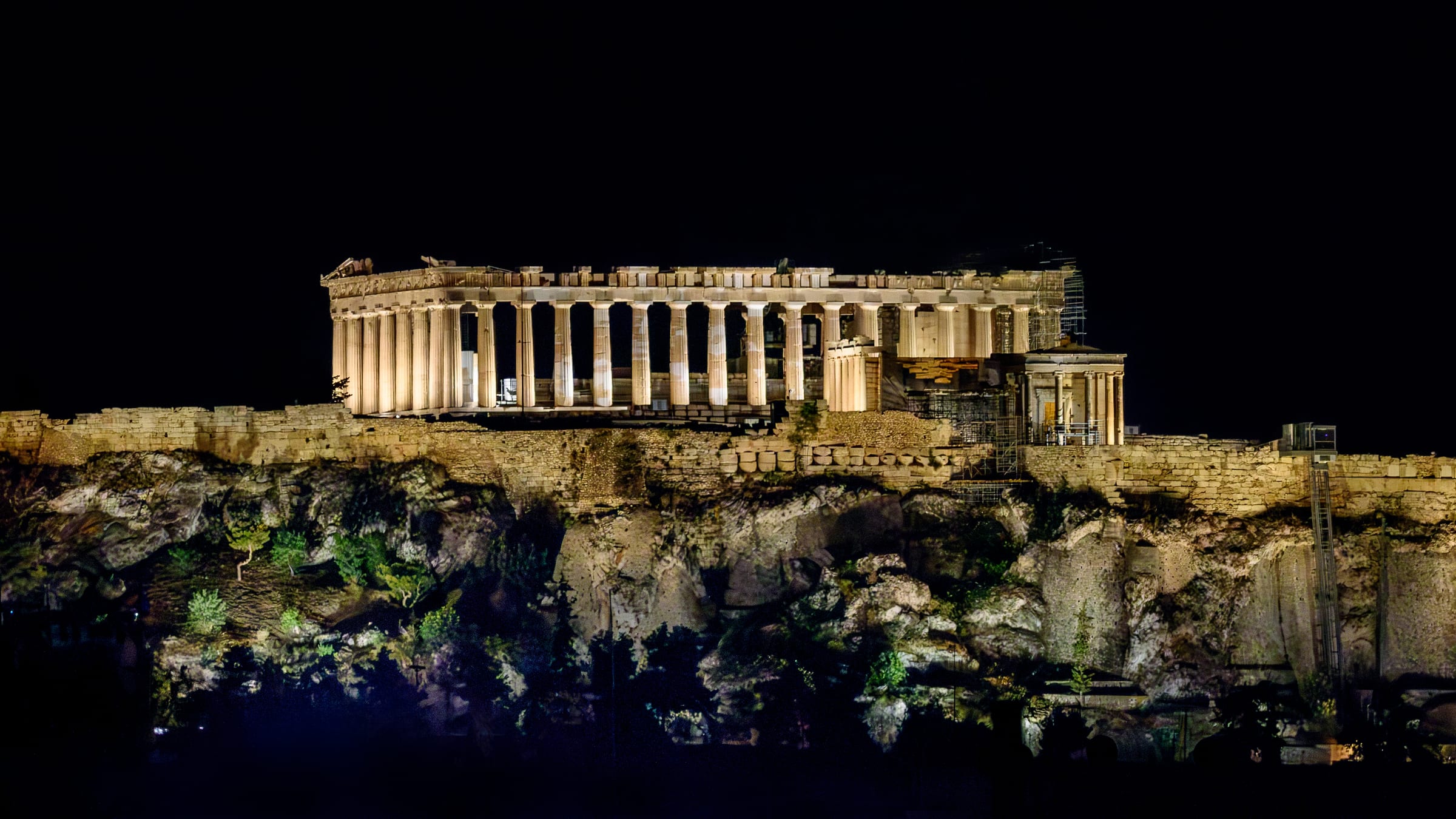 The Acropolis of Athens illuminated at night above the city.
