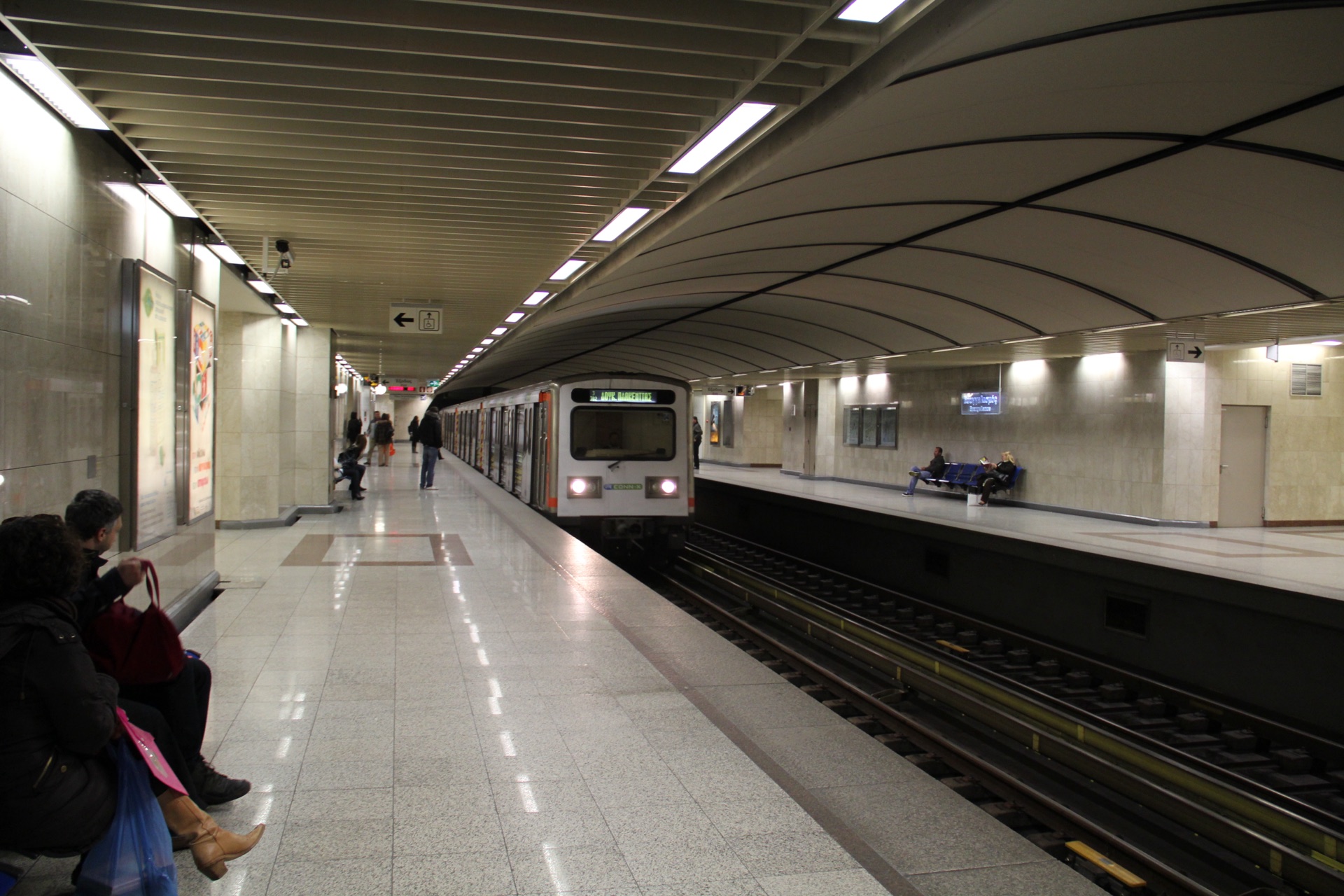 An Athens Metro train arriving at Evangelismos station, with passengers waiting on the platform under its vaulted ceiling.