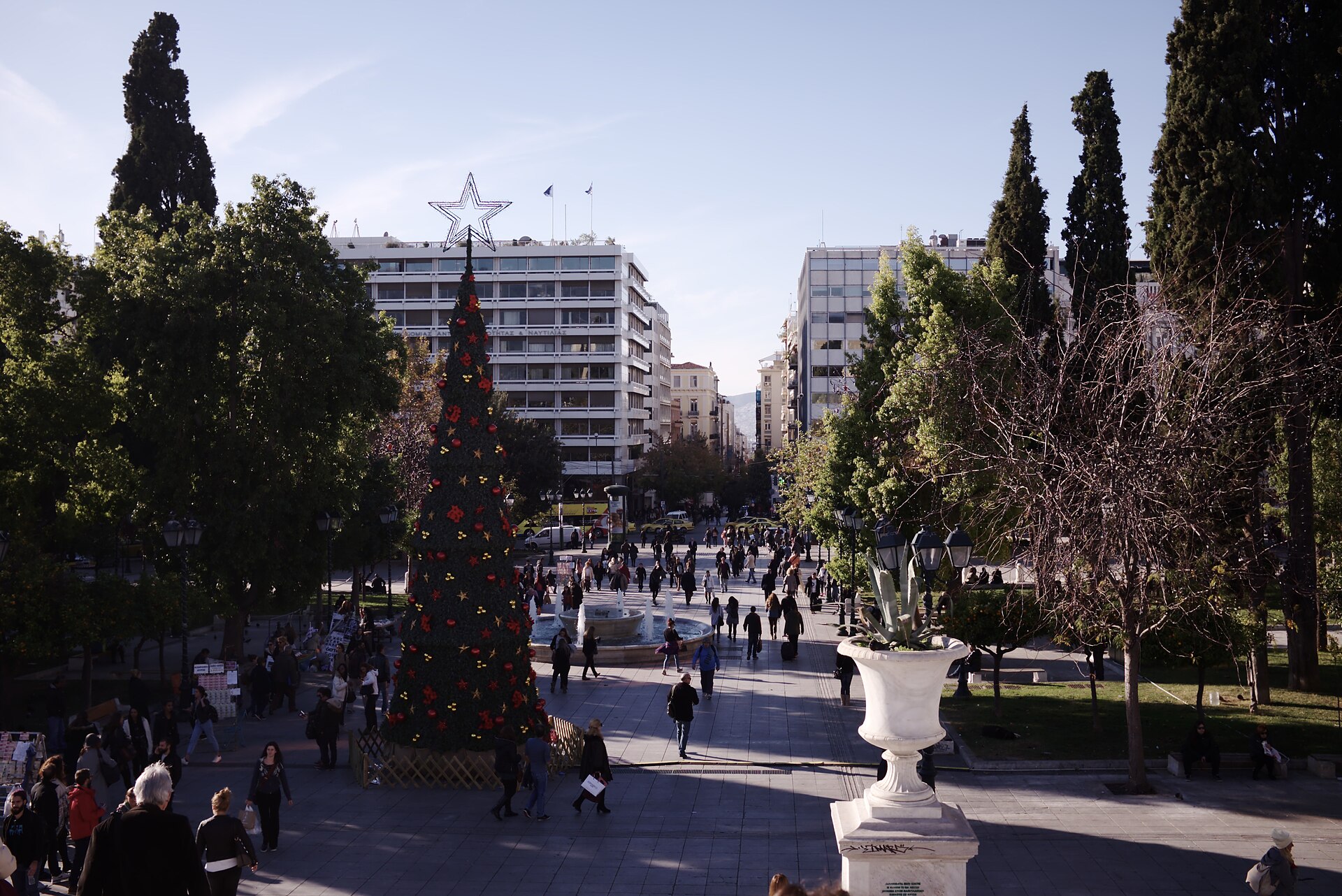 La place Syntagma, dans le centre d'Athènes, avec ses arbres, sa circulation et la ville qui s'élève en arrière-plan.